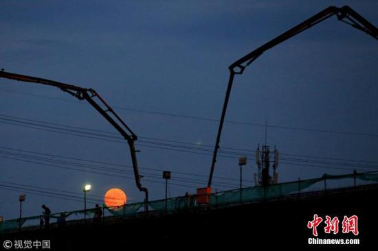 7月27日，江苏省淮安市，建筑工人在月全食前期的红月下施工，构成一幅优美的剪影。周长国 摄 图片来源：视觉中国