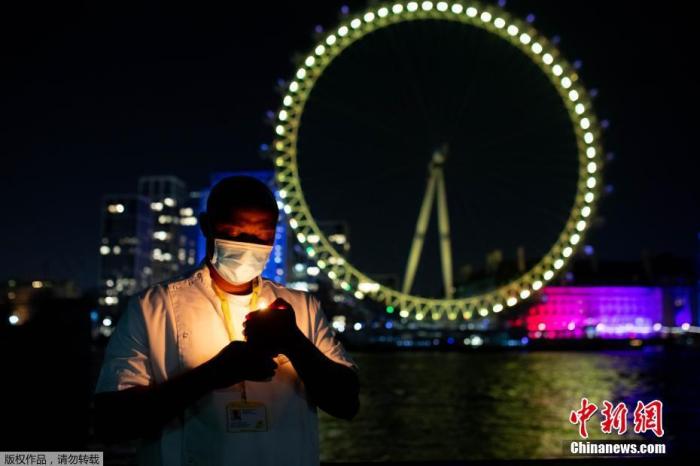 当地时间2021年3月23日，英国伦敦，英国地标和建筑亮起黄色灯光，纪念首次“封城”一周年。图为位于泰晤士河畔的伦敦眼亮起黄灯。