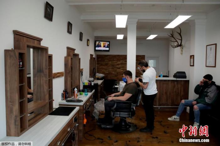 资料图：当地时间4月12日，英国赫特福德一家理发店内，理发师为顾客服务。