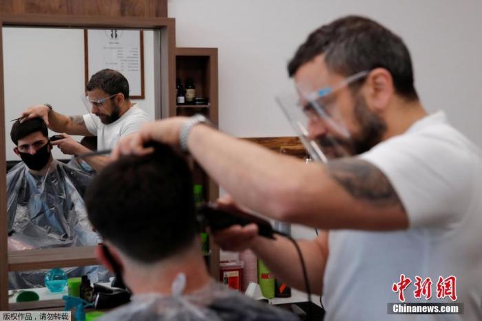 当地时间4月12日，英国赫特福德一家理发店恢复营业，理发师给顾客修剪发型。