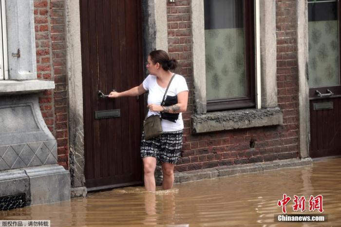 当地时间7月15日，比利时霍格努尔市，一名女士站在家门口被洪水淹没的道路上。