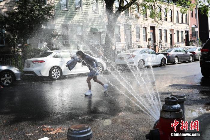 当地时间7月16日，纽约布鲁克林街道上部分消防栓喷水为市民消暑，一名女孩戏水。当日，美国纽约出现36摄氏度高温，纽约市部分街区打开消防栓喷水为市民消暑。 中新社记者 廖攀 摄
