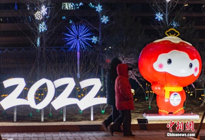 1月20日晚间，位于北京市海淀区五塔寺路的“冰雪廊道”景观亮灯，市民途经北京2022年冬残奥会吉祥物“雪容融”造型。中新社记者 侯宇 摄