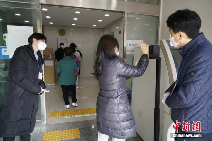 图为首尔市钟路区一投票站门口，选民在工作人员监督下测量体温。 中新社记者 刘旭 摄