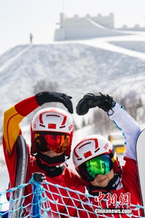 3月10日上午，参加北京2022年冬残奥会残奥单板滑雪坡面回转项目的各国选手在张家口云顶滑雪公园进行赛前训练。图为中国选手耿焱红(左)和王心雨等待出发时向镜头“比心”。 中新社记者 侯宇 摄